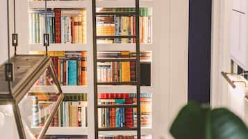 Una estantería llena de libros, una lámpara de pie y una planta grande en una habitación con suelo de madera.