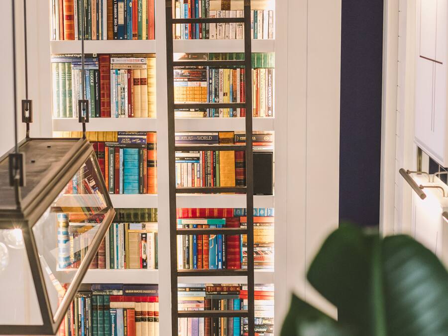 Una estantería llena de libros, una lámpara de pie y una planta grande en una habitación con suelo de madera.