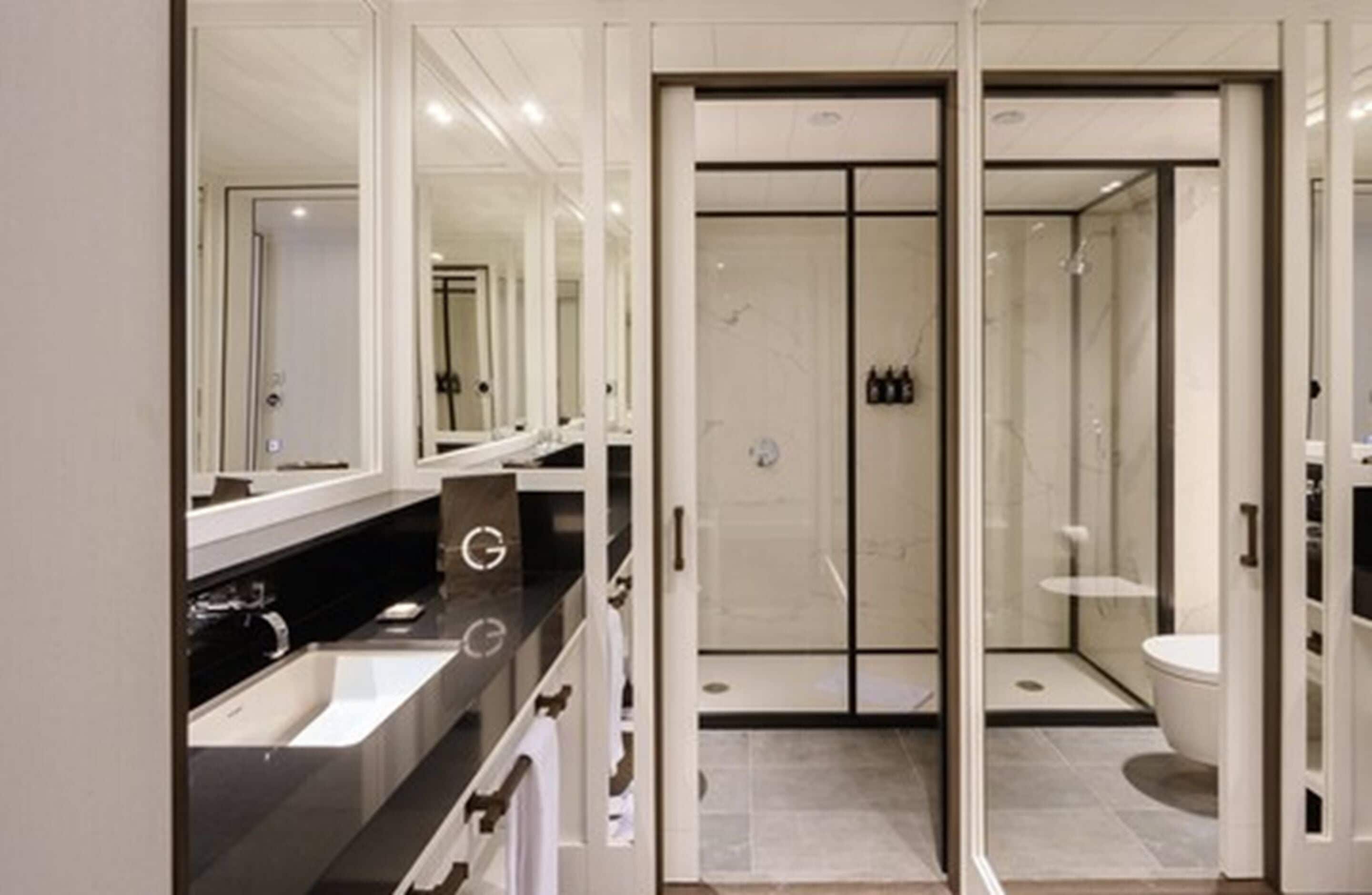 Een moderne badkamer met een grote spiegel, een zwart aanrecht, een douche en een toilet.