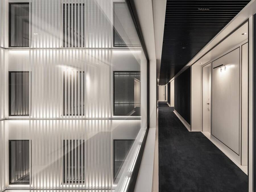 Un couloir d’hôtel moderne avec des murs réfléchissants, une moquette sombre et un design de plafond épuré.