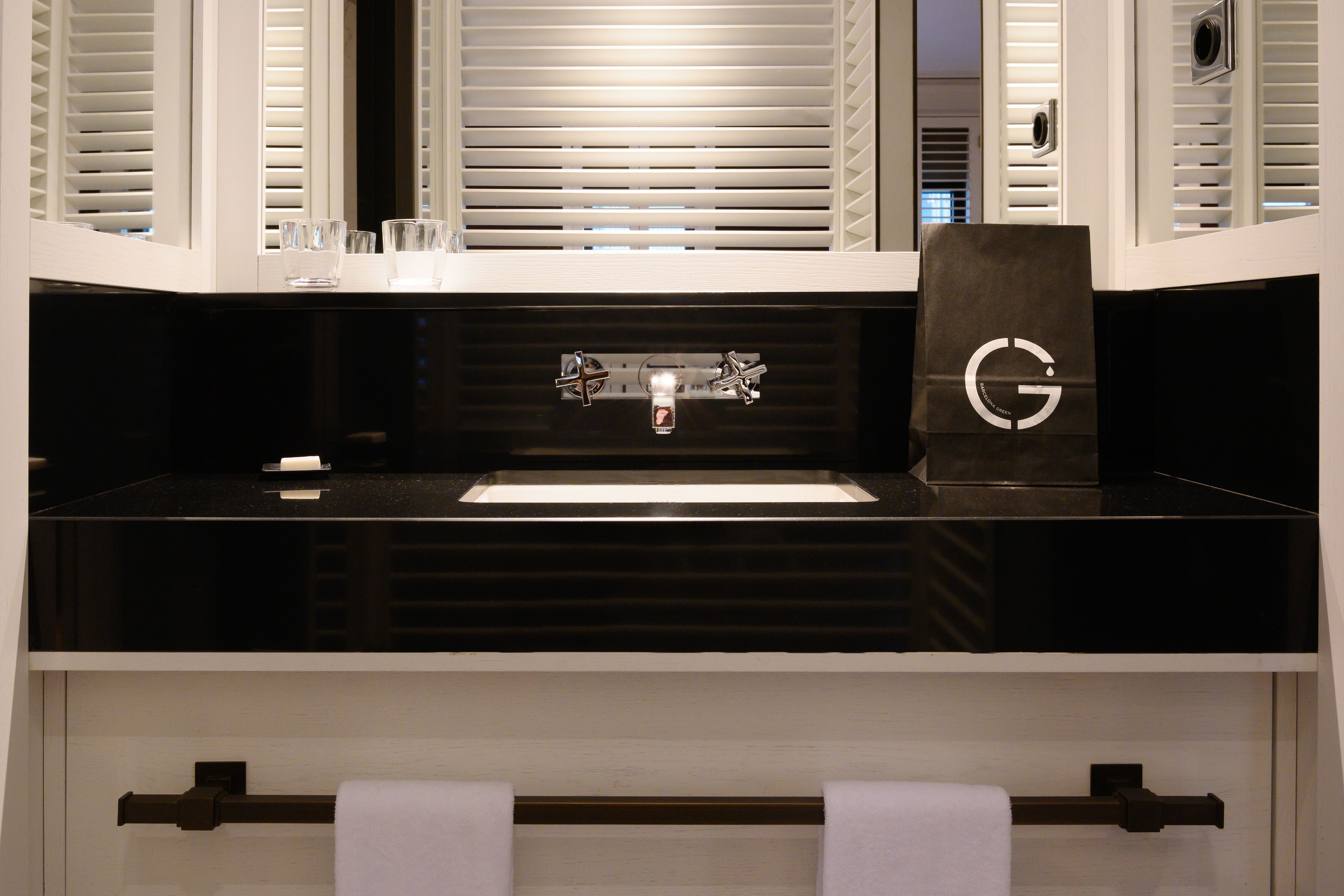 Un baño moderno con un lavabo negro, dos grifos y un perchero con dos toallas blancas.