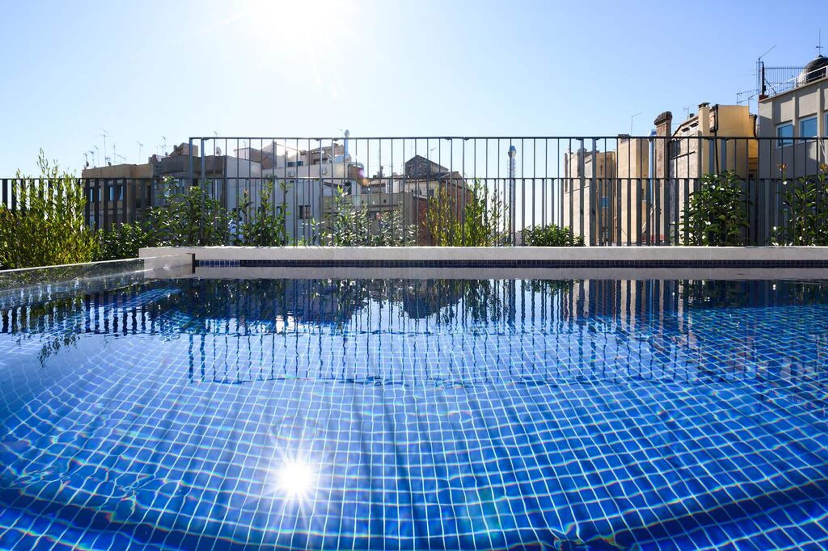 Piscina con superficie de azulejos, rodeada por una valla metálica y vegetación.