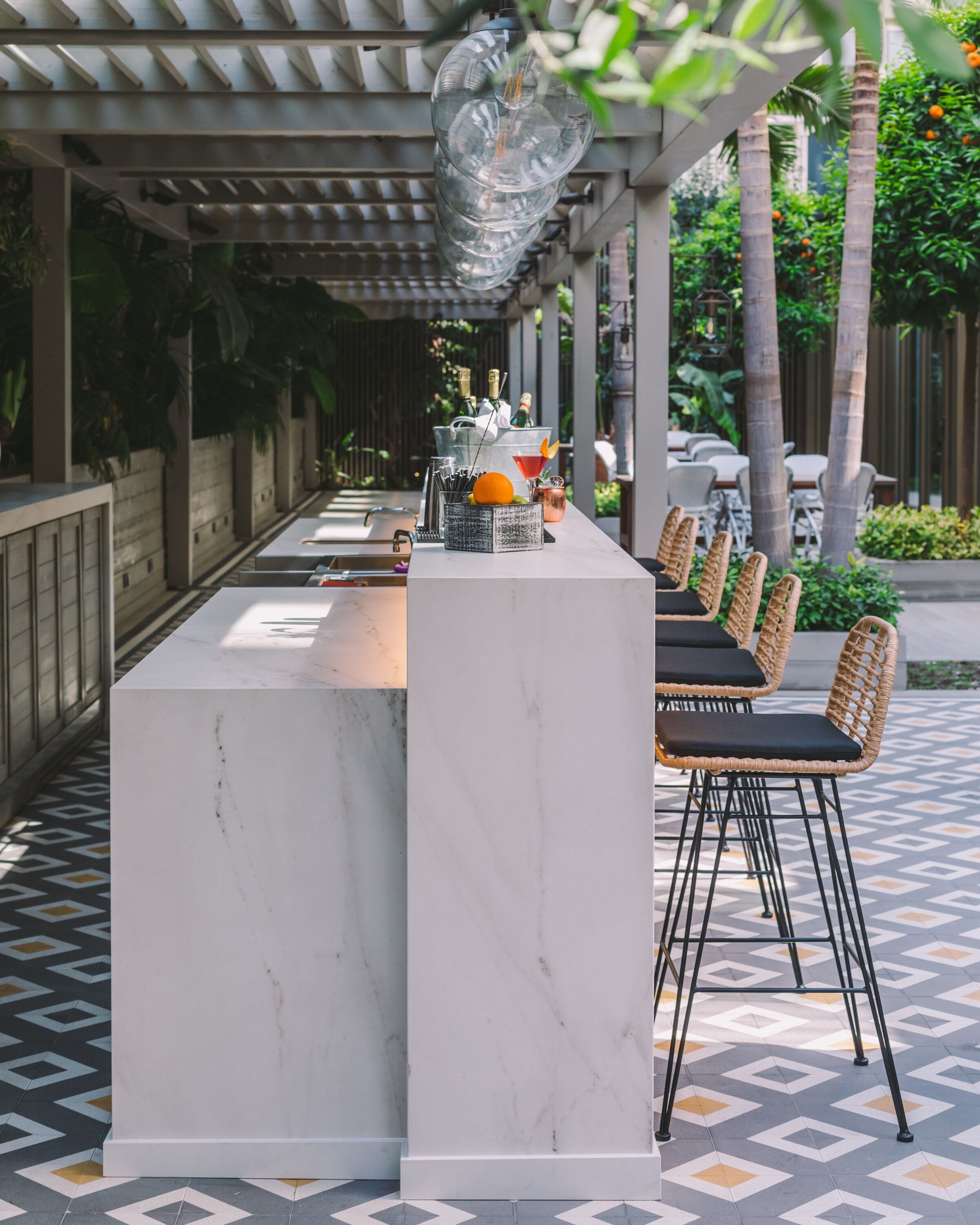 A covered outdoor bar area with a marble countertop, wicker chairs, and a decorative hanging light fixture.