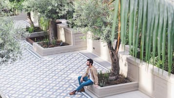 A man sitting on a tiled patio with geometric patterns, surrounded by greenery and a brick wall.