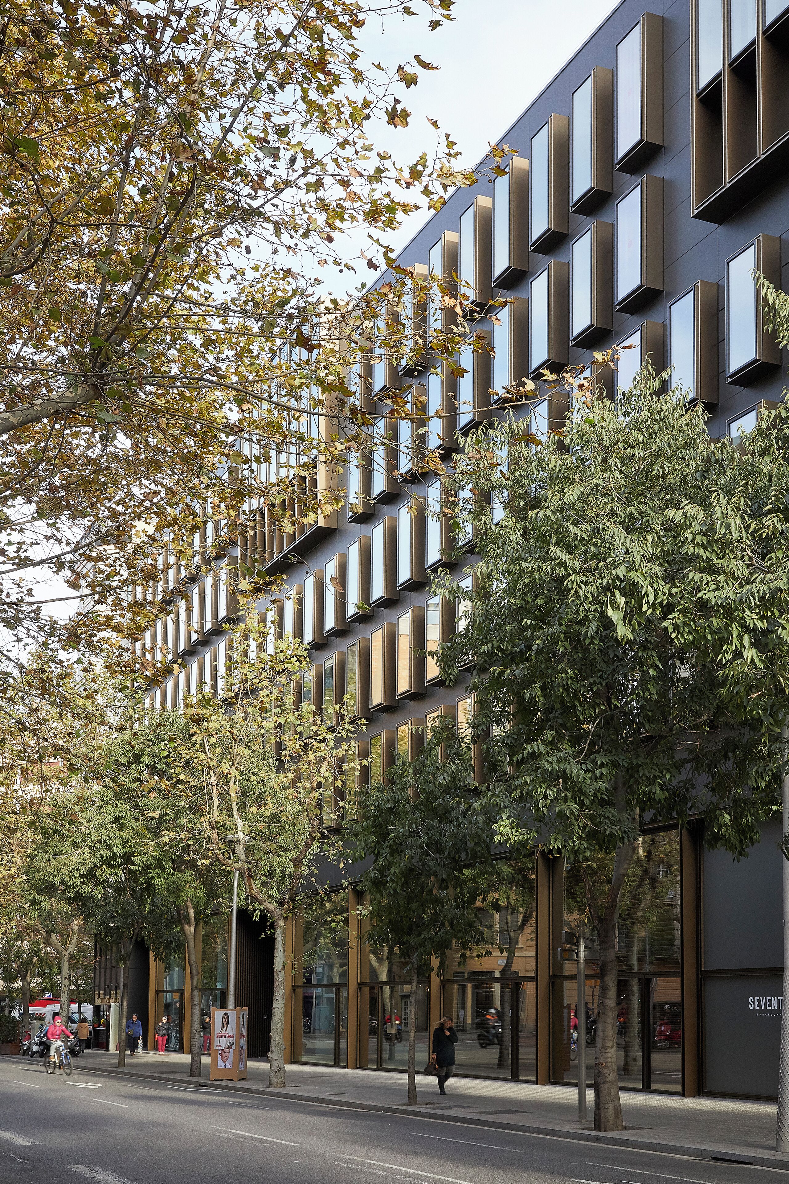 Um edifício moderno com vários janelões retangulares e uma rua arborizada.