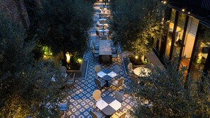 Un patio exterior con mesas y sillas, rodeado de árboles y un suelo con diseño.