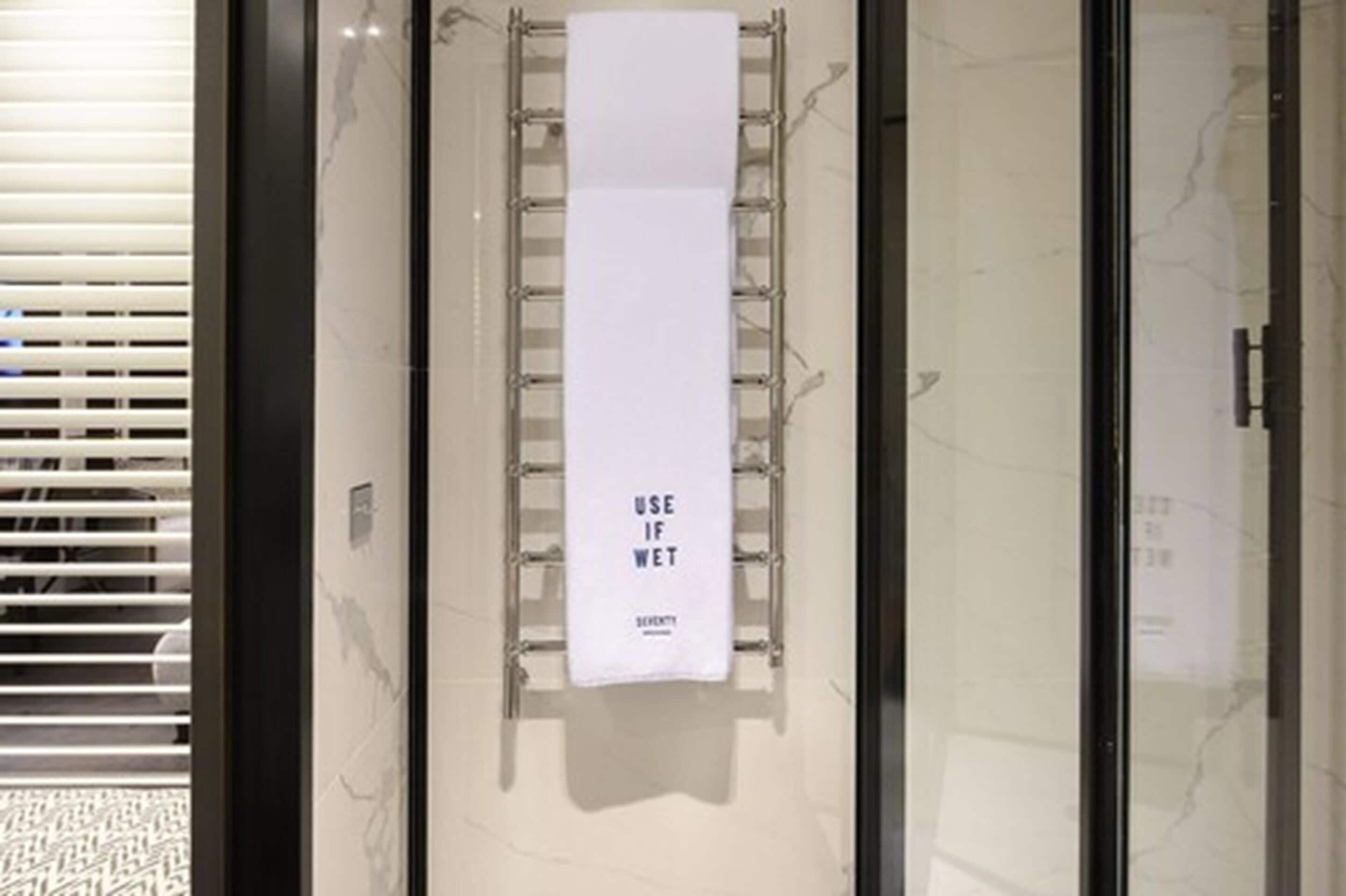 A bathroom with a towel rack holding a white towel with the text "USE IF WET" and a glass shower door.