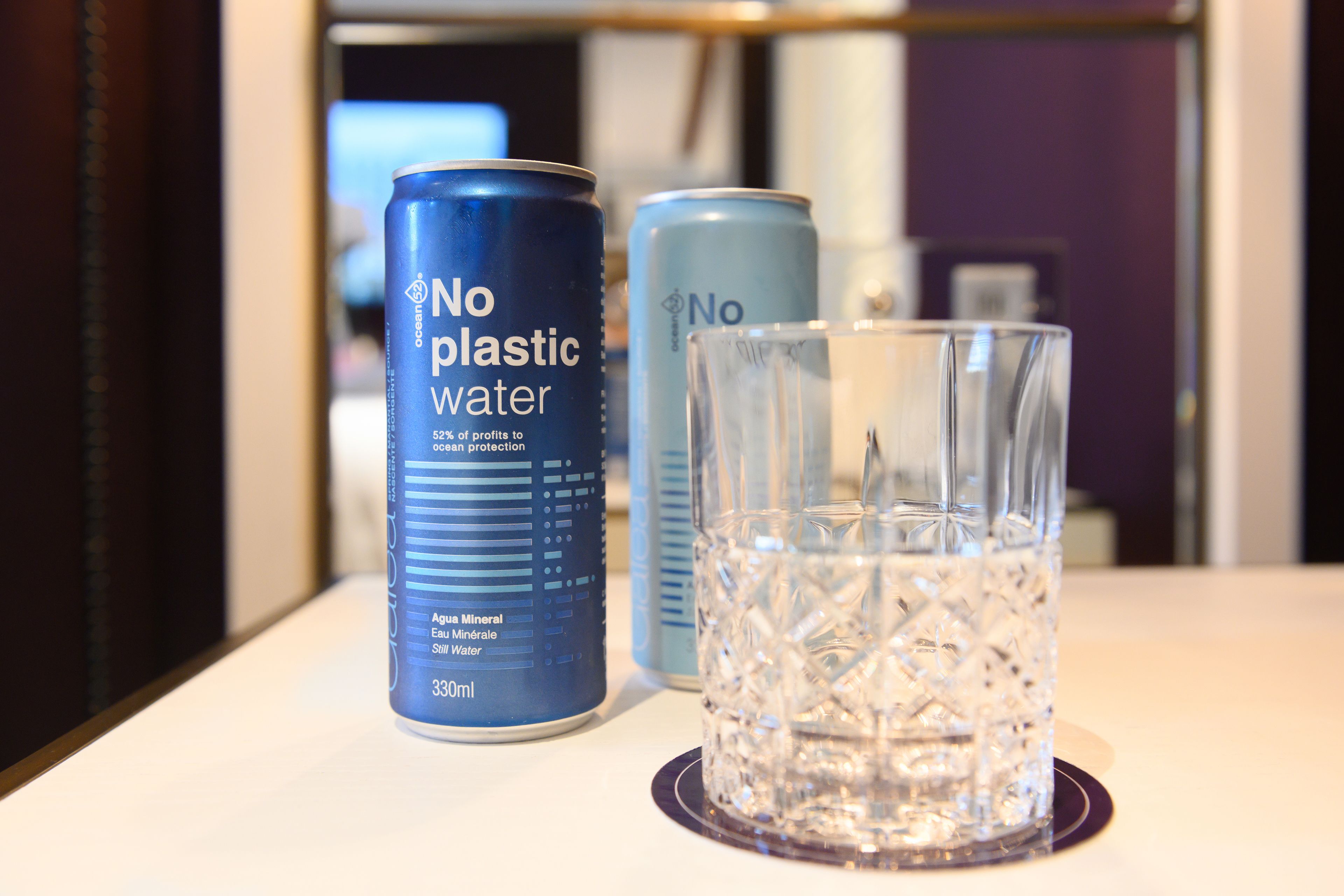 Two cans of 'No Plastic Water' and a glass on a table.