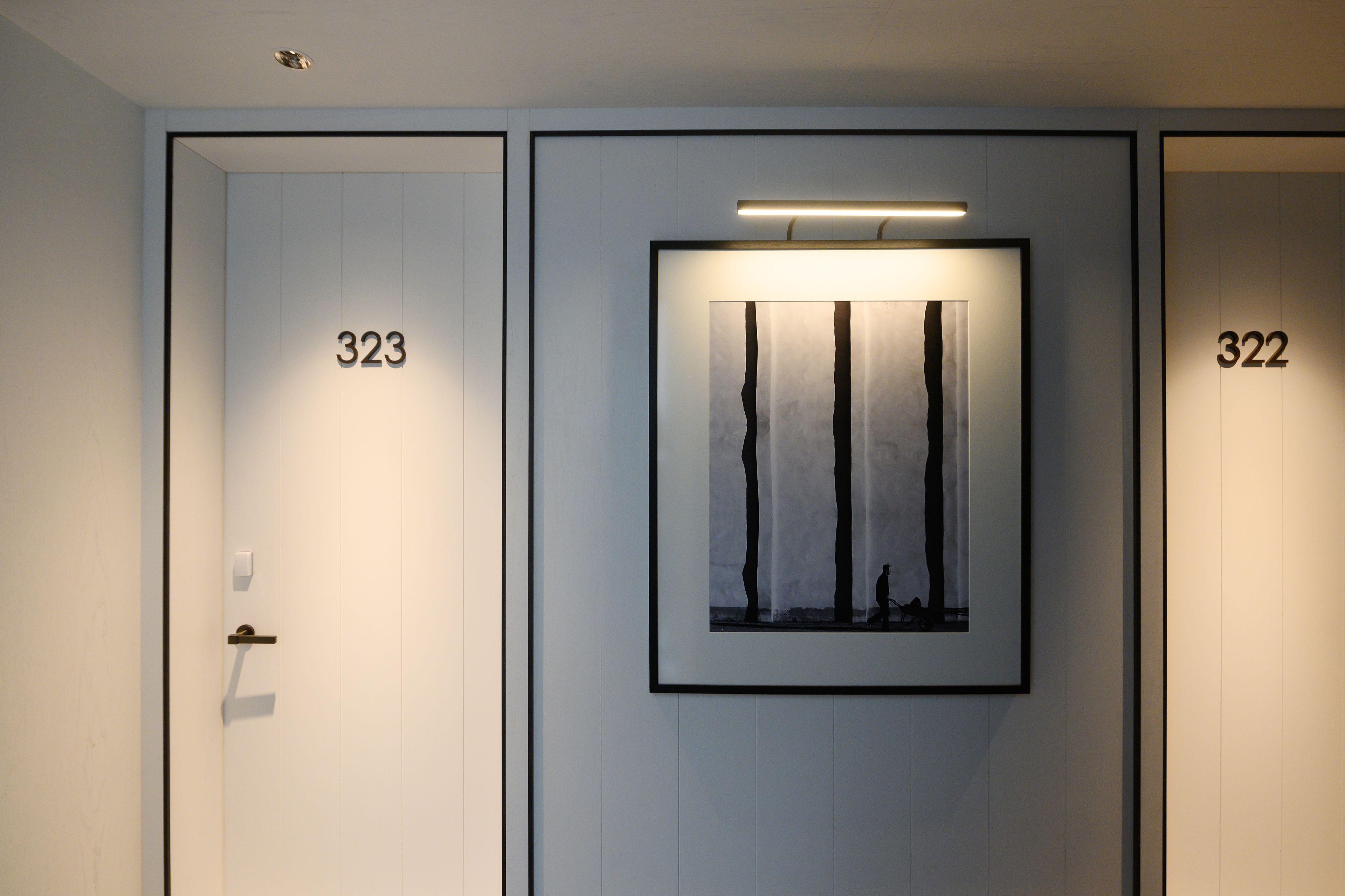 A hotel room with doors numbered 323 and 322, a framed artwork on the wall, and a light fixture above it.