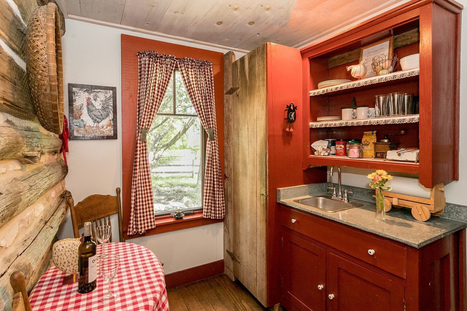 A rustic kitchen with a wooden table, checkered curtains, and a sink.