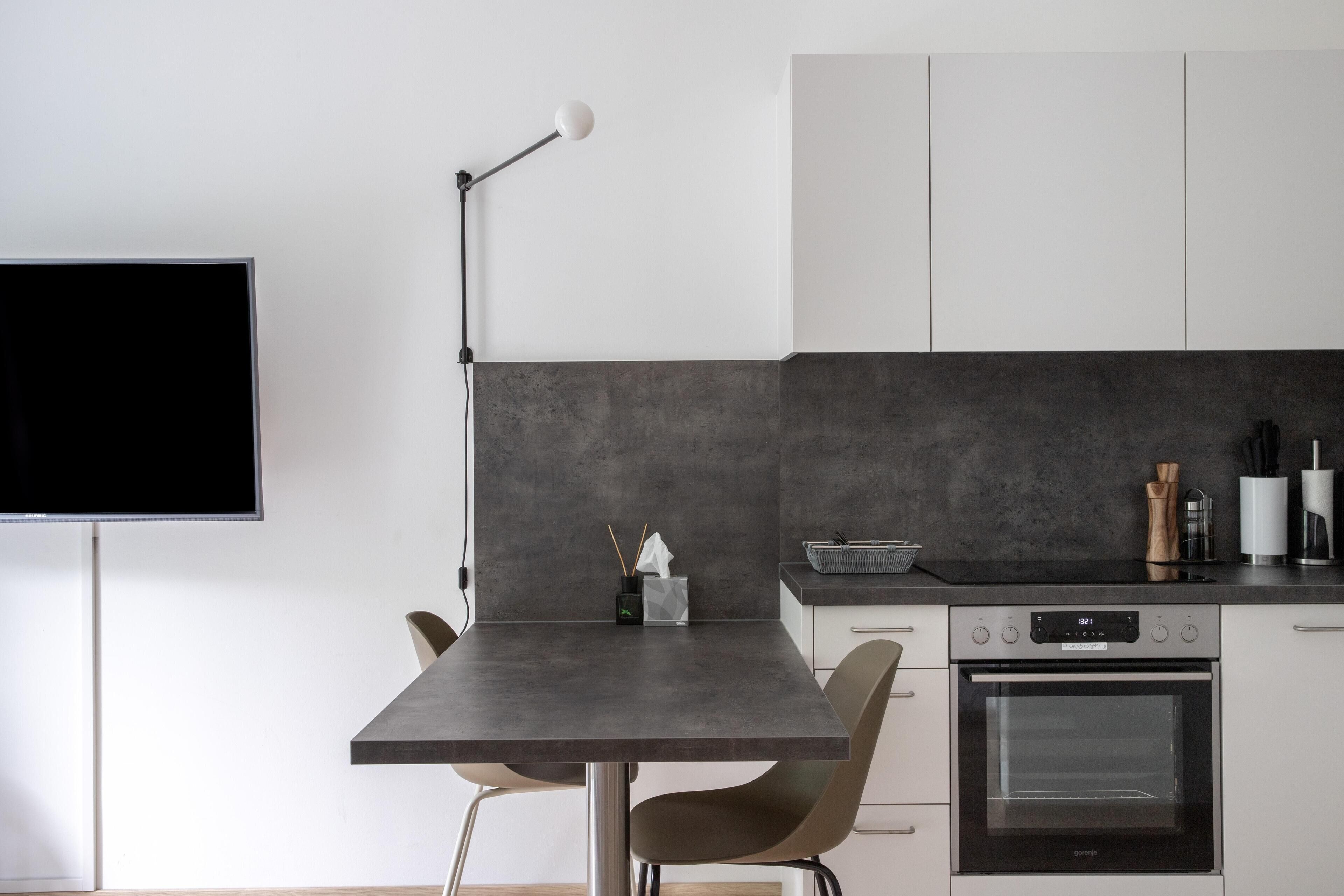 A modern kitchen with a dark countertop, a built-in oven, and a wall-mounted TV.