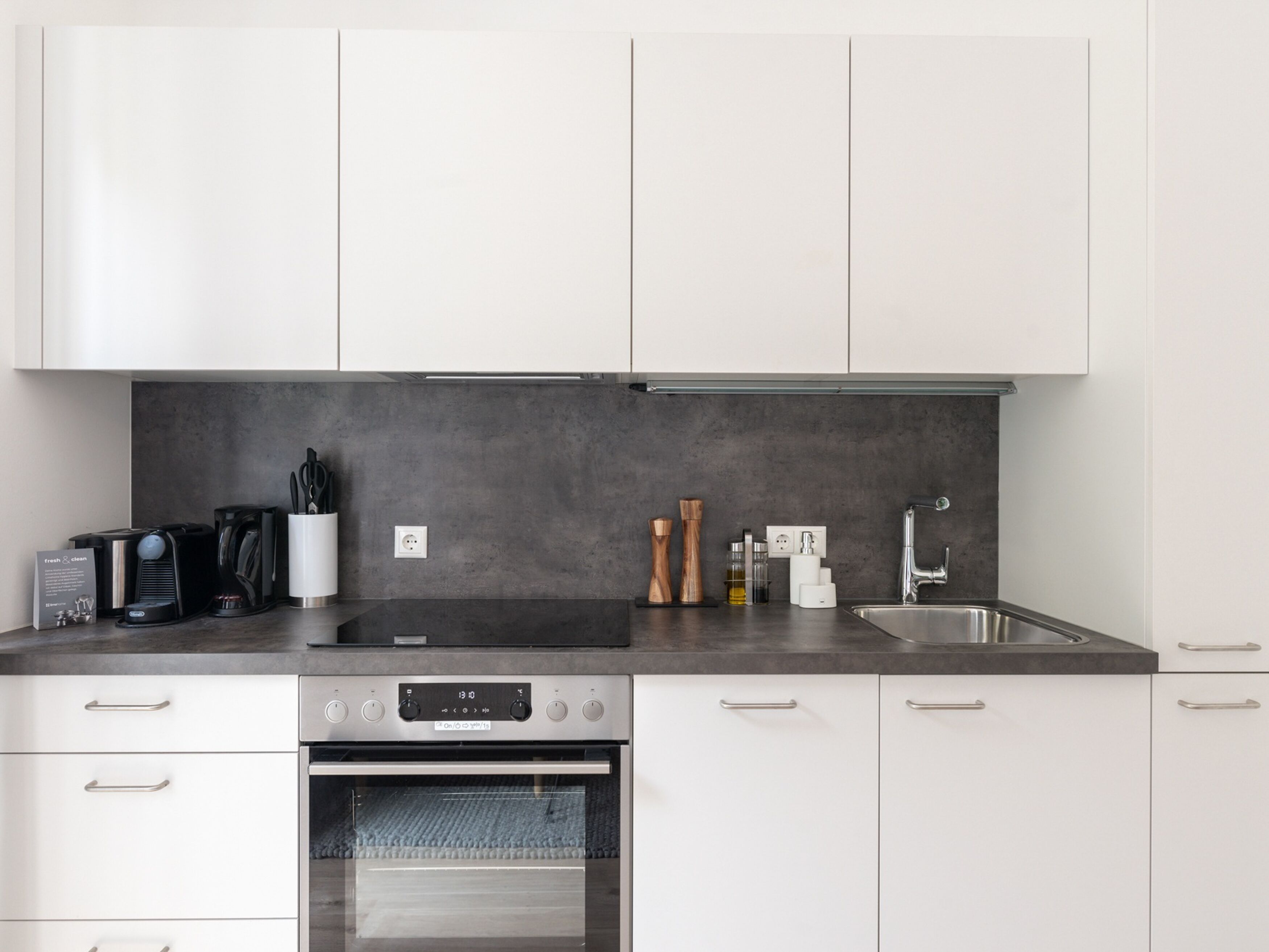 A modern kitchen with white cabinets, a stainless steel sink, and a built-in oven.