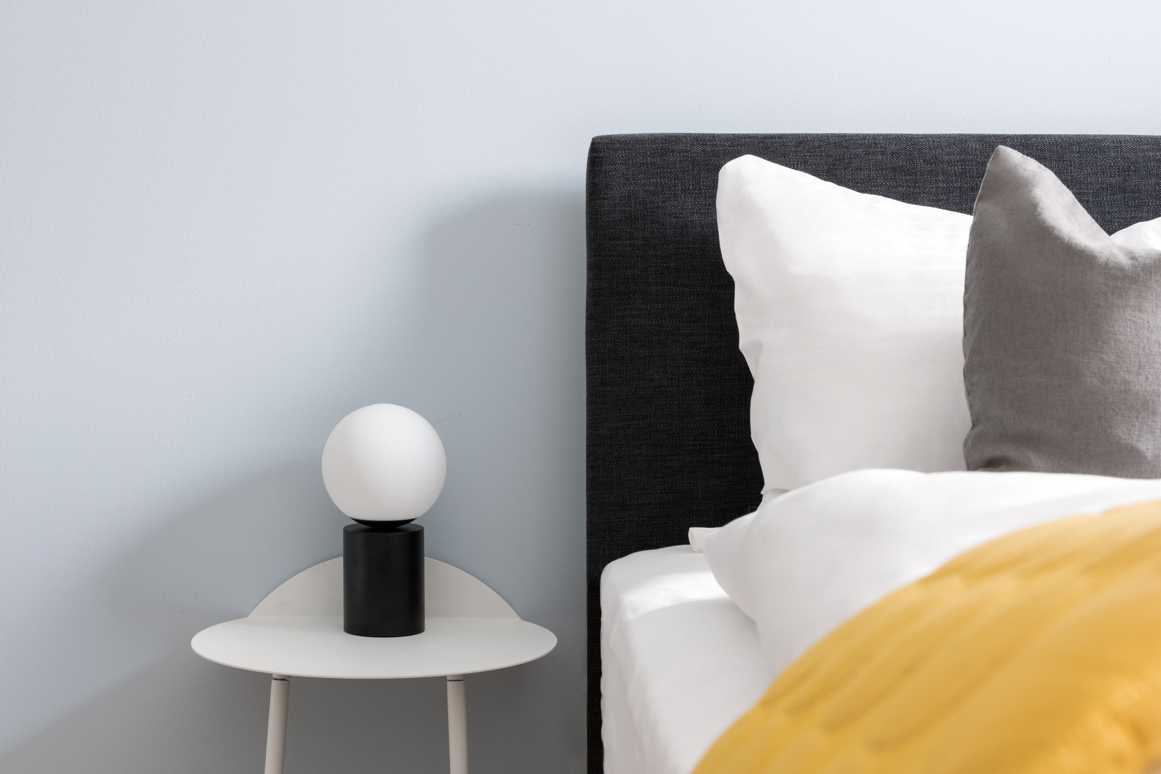 Une chambre à coucher moderne avec un lit, une table de chevet sur laquelle se trouve un objet sphérique, et une commode.