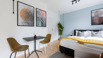Una habitación de hotel moderna con una cama, un escritorio, dos sillas y obras de arte en las paredes.