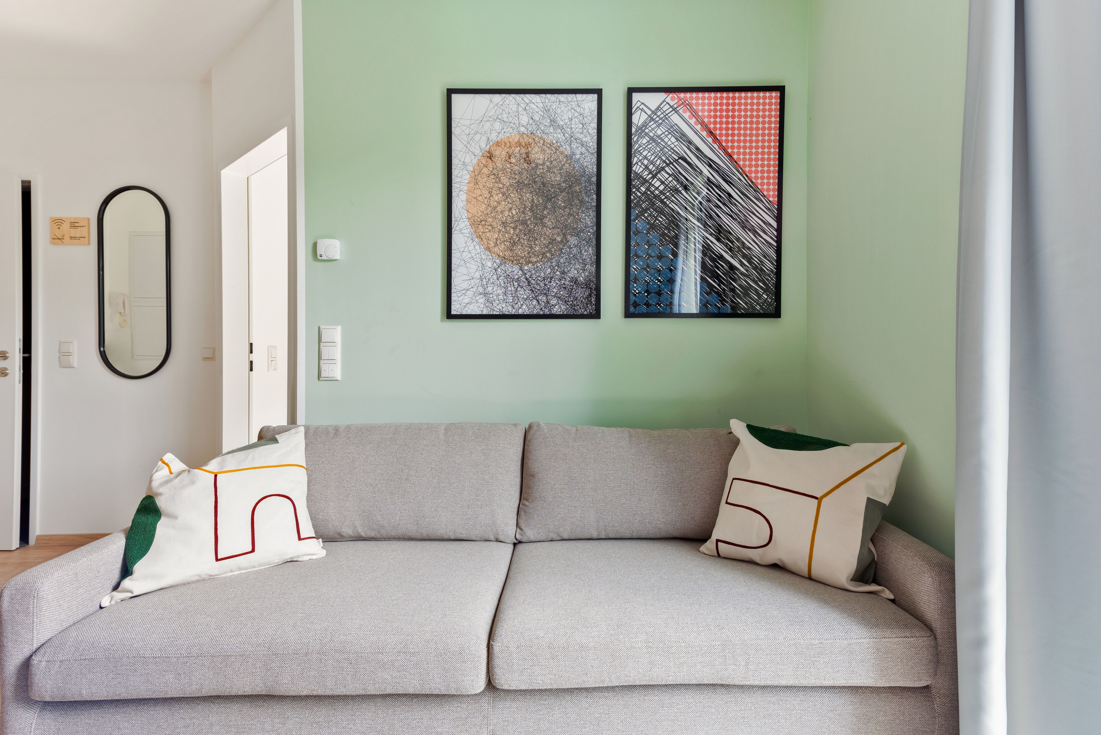 A modern living room with a grey sofa, two framed artworks, and a green wall.