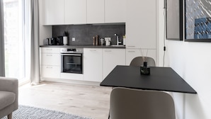 Cocina moderna con armarios blancos, encimera negra y horno empotrado. Hay una mesa de comedor con sillas y un florero negro encima.