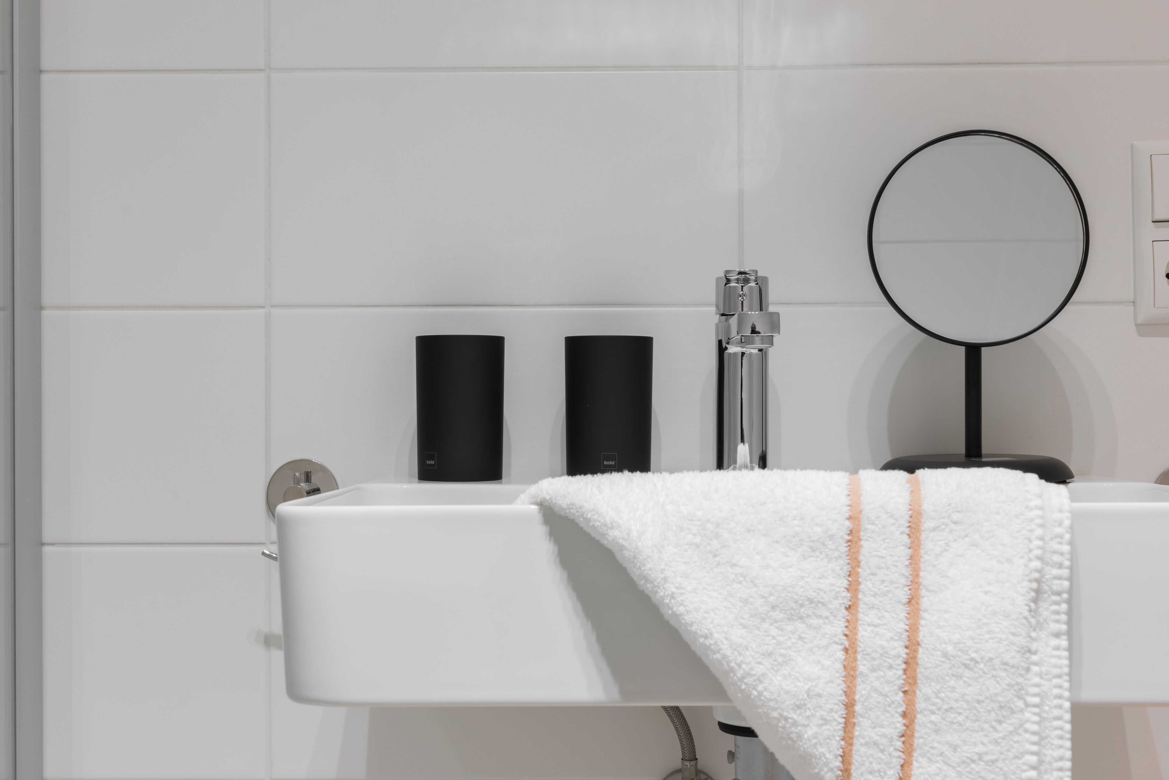 A bathroom with a white sink, black soap dispensers, a mirror, and a towel.
