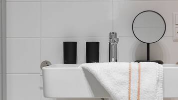 A bathroom with a white sink, black soap dispensers, a mirror, and a towel.