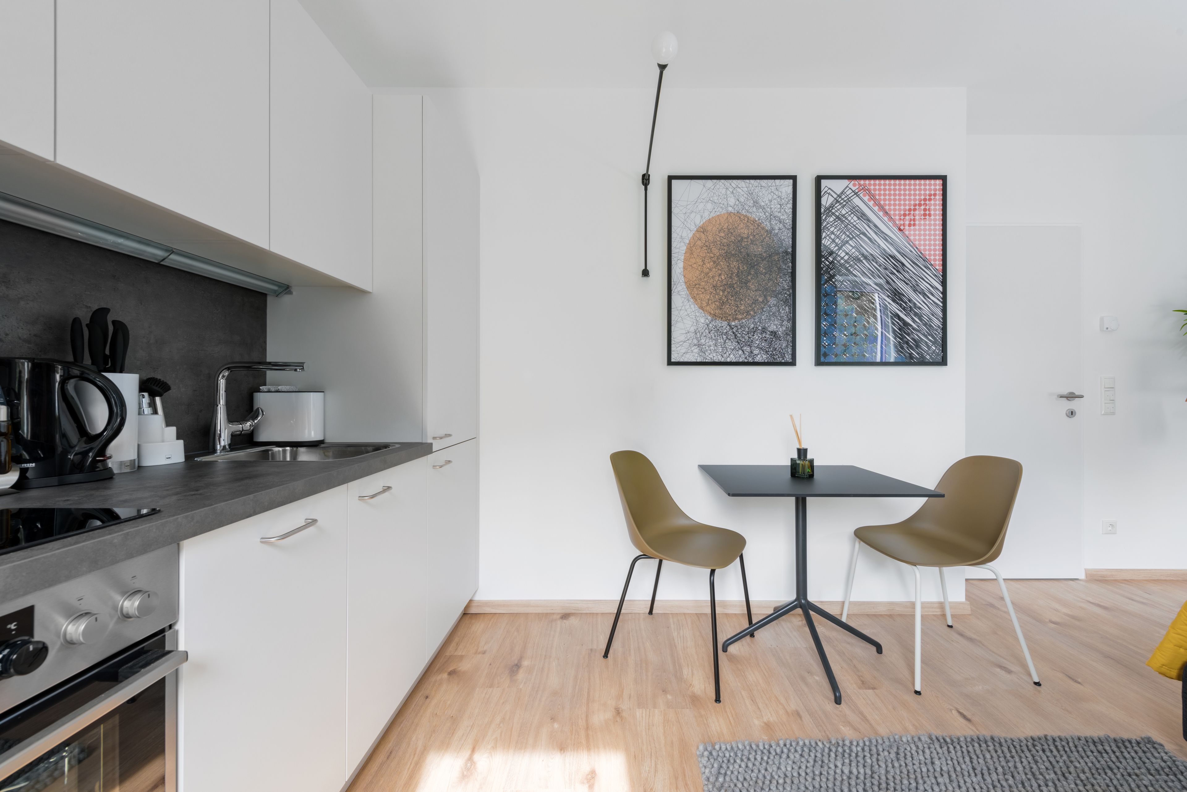 Eine moderne Küche mit weißen Schränken, einer schwarzen Arbeitsplatte und einem Essbereich mit zwei Stühlen und einem Tisch.
