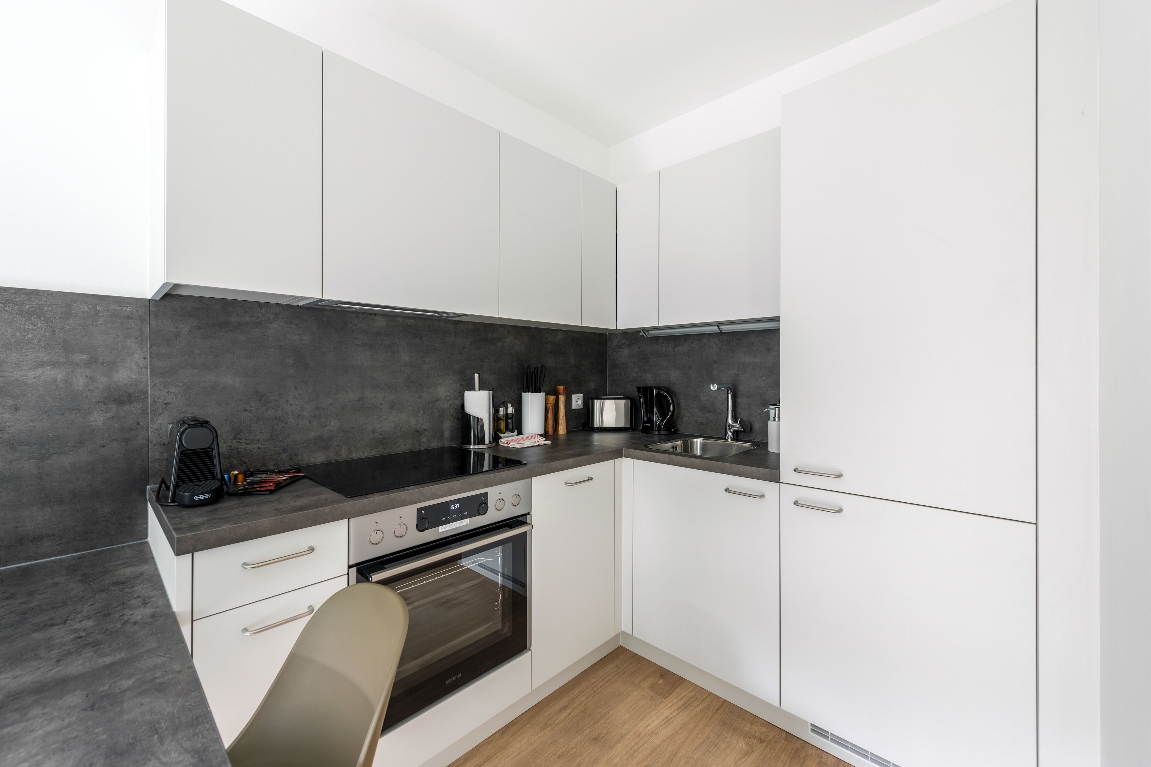 A modern kitchen with white cabinets, a black countertop, a built-in oven, and a sink.
