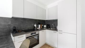 A modern kitchen with white cabinets, a black countertop, a built-in oven, and a sink.