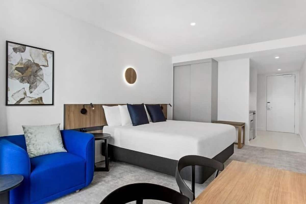 Une chambre d’hôtel moderne avec un grand lit, un canapé bleu, une applique murale ronde et une œuvre d’art abstraite encadrée.