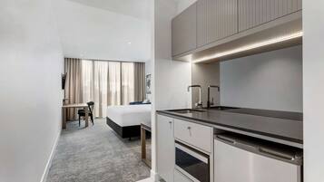 A modern hotel room with a kitchenette, a bed, a desk, and a window with curtains.