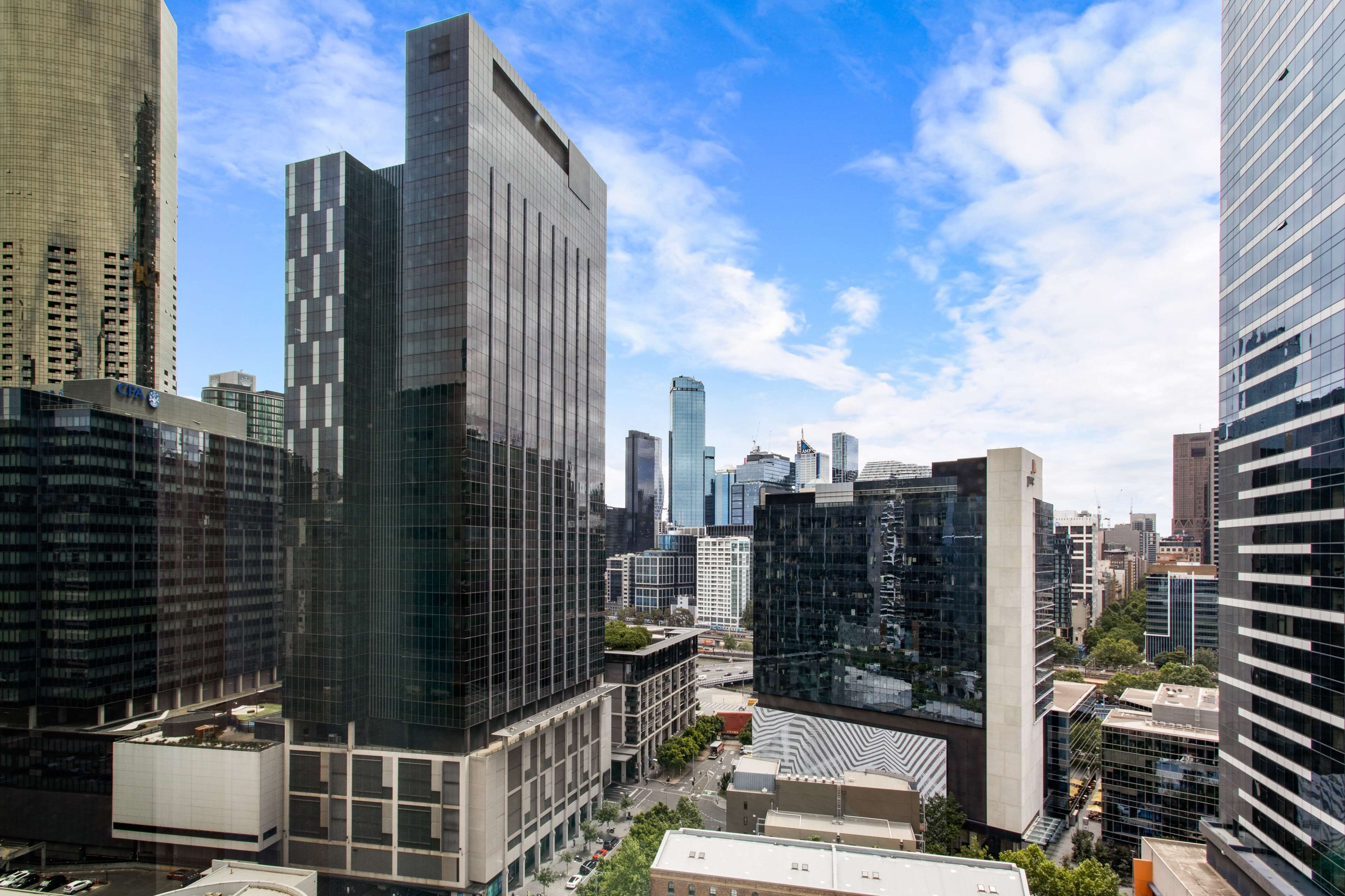 A cityscape with modern high-rise buildings, including a prominent glass skyscraper and a building with a unique geometric facade.