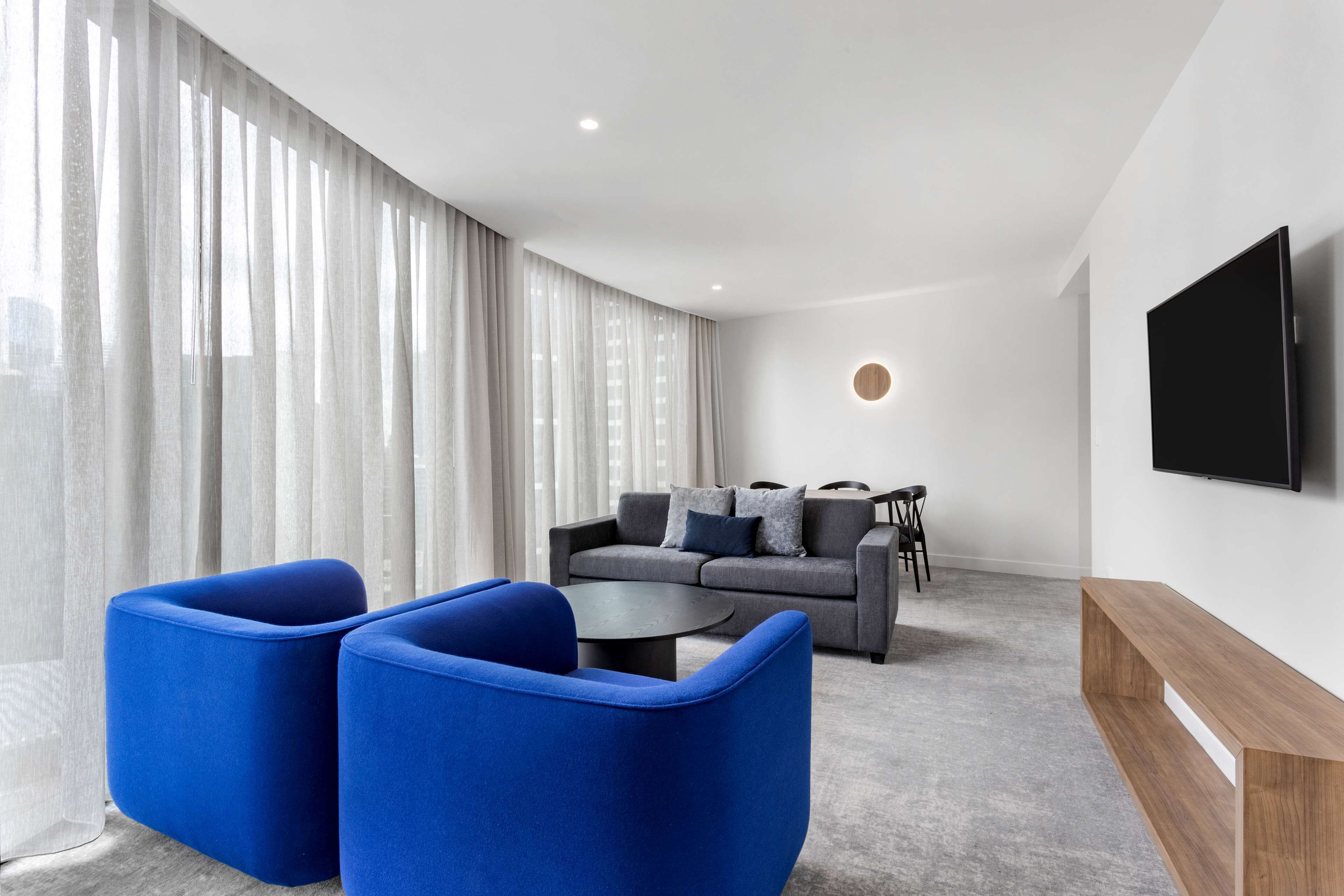Un soggiorno moderno con un divano grigio, poltrone blu, un tavolino da caffè e una TV a parete.