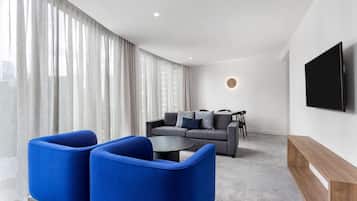 A modern living room with a grey sofa, blue armchairs, a coffee table, and a TV mounted on the wall.