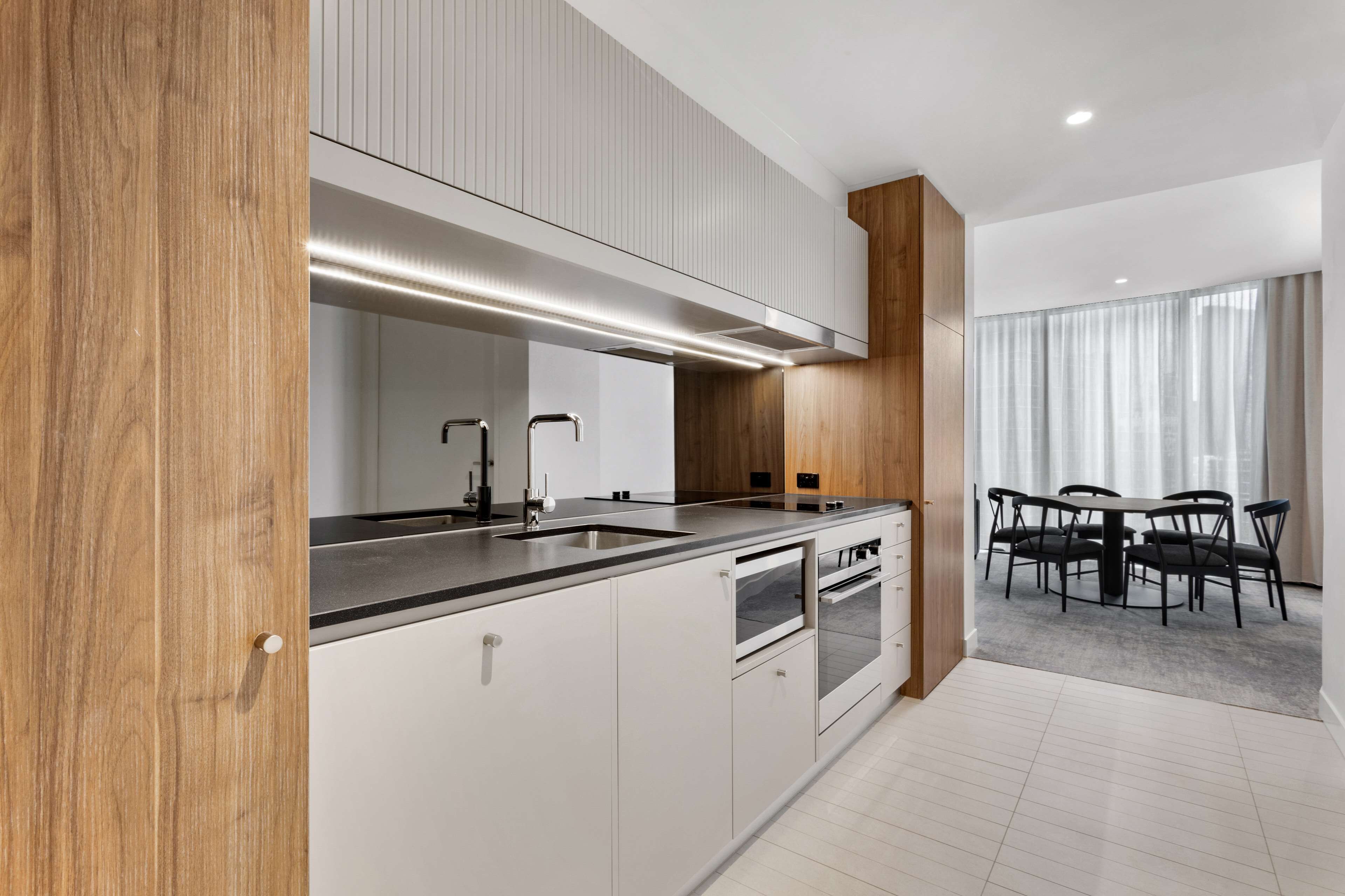 A modern kitchen with a large island, built-in oven, and a dining area with a table and chairs.