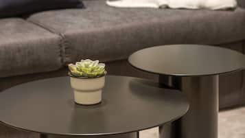 Una sala de estar moderna con un sofá gris, una manta blanca y una pequeña planta en una mesita redonda negra.