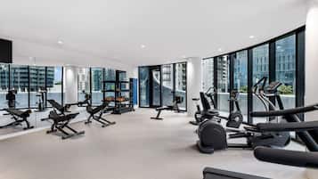 A modern gym with various exercise equipment, large windows, and a view of high-rise buildings.