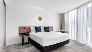 A modern hotel room with a large bed, a round wall light, a small side table, and sheer curtains.