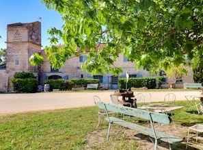 A courtyard with a stone building, outdoor seating, and a tree providing shade.