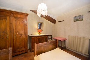 Une chambre à coucher avec une armoire en bois, un bureau avec une lampe, une chaise, un lit et un radiateur.
