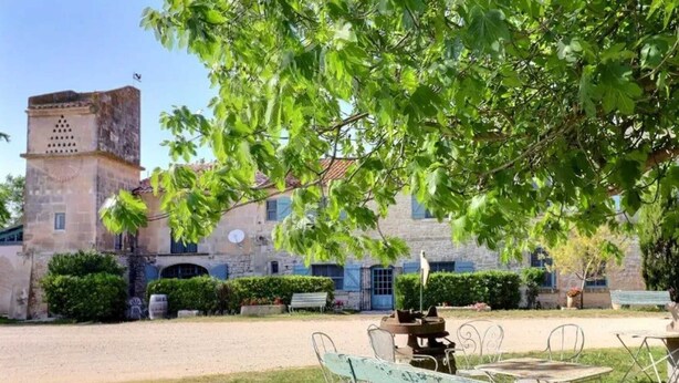 A courtyard with stone buildings, a tower, and outdoor seating under a tree. - Homerez - House near Saintes-Maries-de-la-Mer (Saintes-Maries-de-la-Mer)