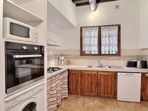 Une cuisine équipée d’un four, d’un micro-ondes et d’un lave-vaisselle intégrés, de placards en bois et d’une fenêtre avec des rideaux.