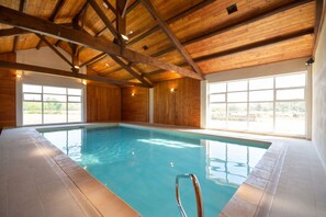 Une piscine intérieure avec des poutres en bois et de grandes fenêtres.