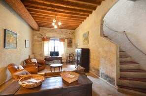 Un intérieur rustique avec un plafond en bois, des murs en pierre, un escalier, des canapés en cuir, un téléviseur et une cheminée.