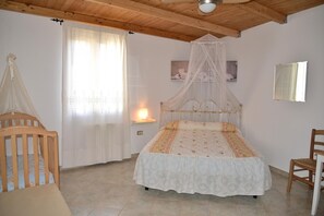 A bedroom with a canopy bed, a crib, a bedside table with a lamp, and a chair. - B&B S'Incontru (Galtelli)