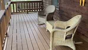 A wooden porch with two wicker rocking chairs and a wooden bench.