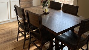 A dining area with a wooden table and chairs, a small vase with flowers, and a view of the outdoors through a window.