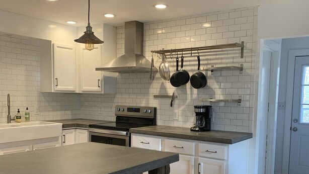 A modern kitchen with white cabinets, a large island with stools, stainless steel appliances, and a hanging pot rack.