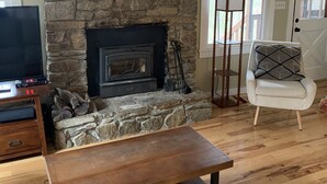 A living room with a stone fireplace, a ceiling fan, a television, and a wooden bench.