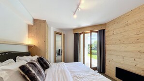 A bedroom with a large bed, wooden panel walls, a ceiling light, and a view of the outdoors through a door.