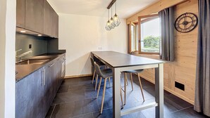 A modern kitchen with dark cabinets, a central island with stools, a hanging light fixture, and a window with curtains.