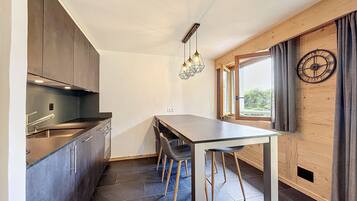 Une cuisine moderne avec des meubles de couleur sombre, un îlot central doté de tabourets, un luminaire suspendu et une fenêtre agrémentée de rideaux.