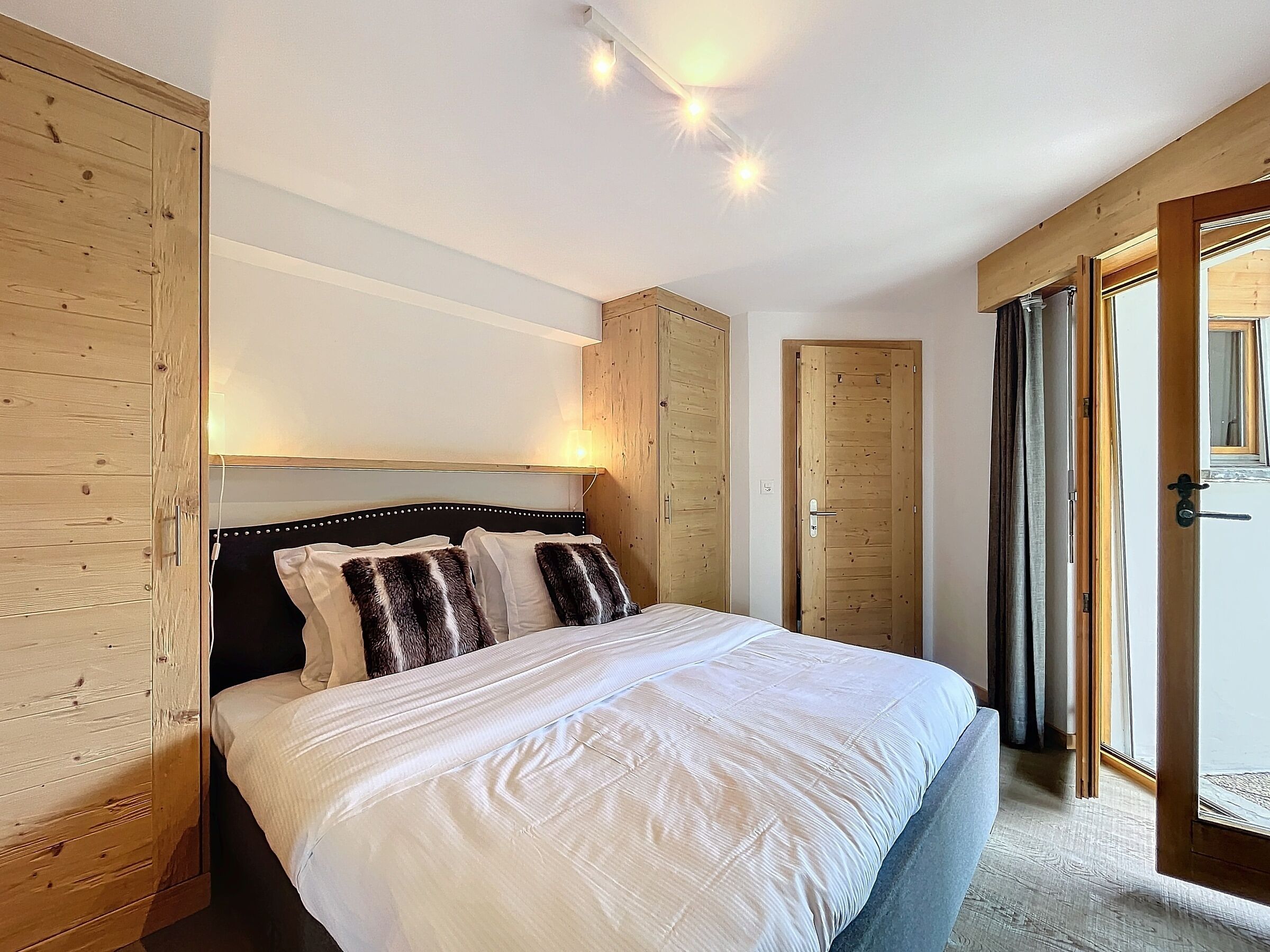 Une chambre avec un grand lit, une armoire en bois et une porte donnant sur un balcon.