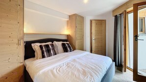 A bedroom with a large bed, wooden wardrobe, and a door leading to a balcony.
